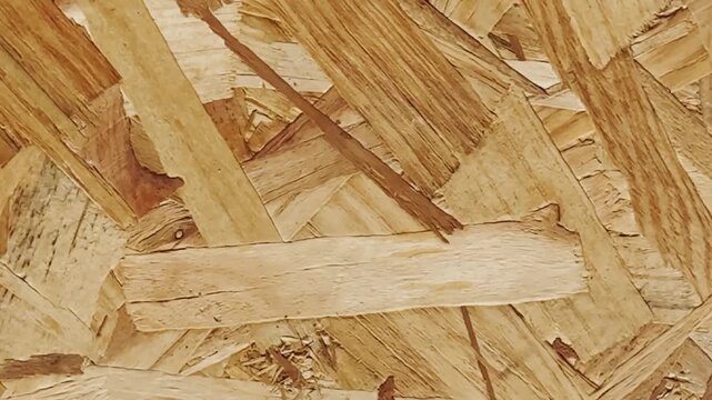 Close-up of oriented strand board with layered wood strands, rough pressed-chip texture, warm beige tones, and construction material surface detail.