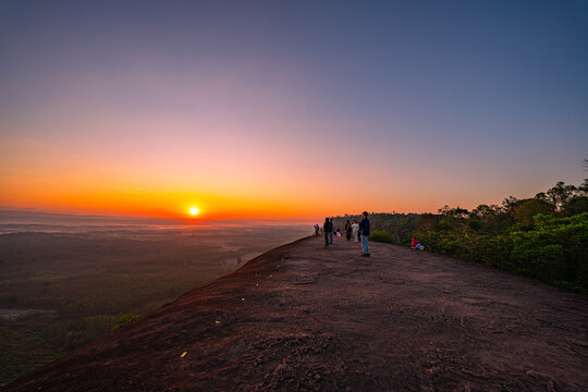 Silhouetted travelers gather on the massive rock formation of Three Whale Rock, watching the first light of day spread across the misty countryside of northeastern Thailand.