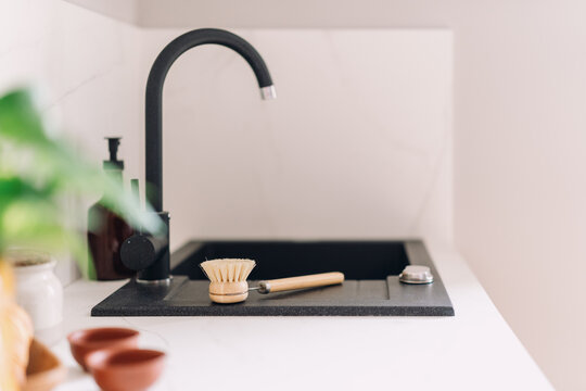 Modern kitchen sink area with black faucet and natural wooden brush