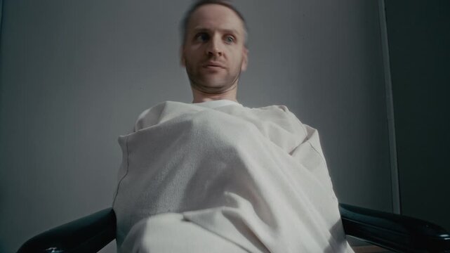 Medium shot of mid aged Caucasian man wearing straitjacket sitting in chair, shaking head frantically and smiling maniacally. Clip is ideal for psychiatric healthcare promos or cinematic horror films