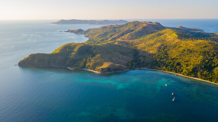 Fototapeta premium Aerial sunset view of tropical rolling hills, turquoise coral reef, and boats in Komodo National Park, Indonesia.