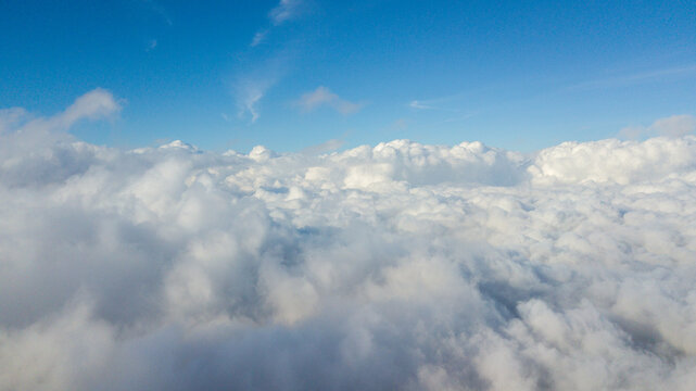 Stunning aerial view above the clouds looking out at a fluffy white cloudscape under a bright blue sky.