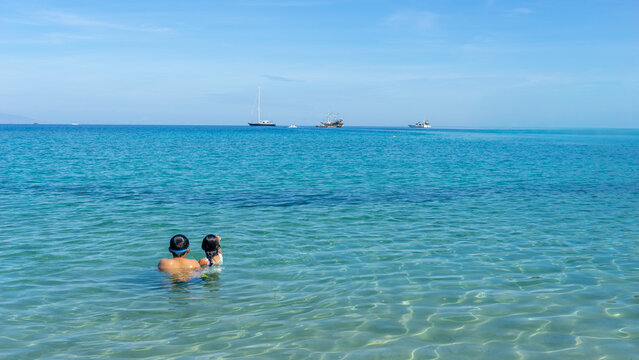 Two Children Swimming in Clear Turquoise Ocean Looking at Distant Boats