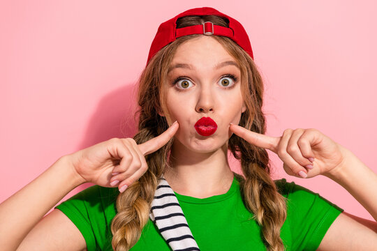 Young woman with red cap making a playful kissy face against pink background in casual fashion lifestyle stock photo