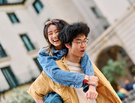 Portrait of a lovely young couple having fun and laughing together piggyback outdoors, tourists travel in the city
