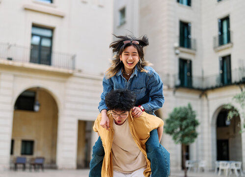 Portrait of a lovely young couple having fun and laughing together piggyback outdoors, tourists travel in the city