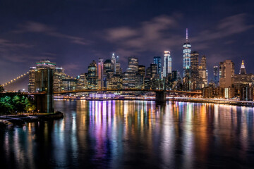 Obraz premium Night City Skyline with Glowing Lights Reflected on Water in Long Exposure Photography