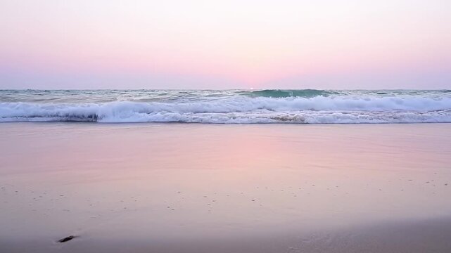 Ocean waves crashing on sandy shoreline at sunset or sunrise