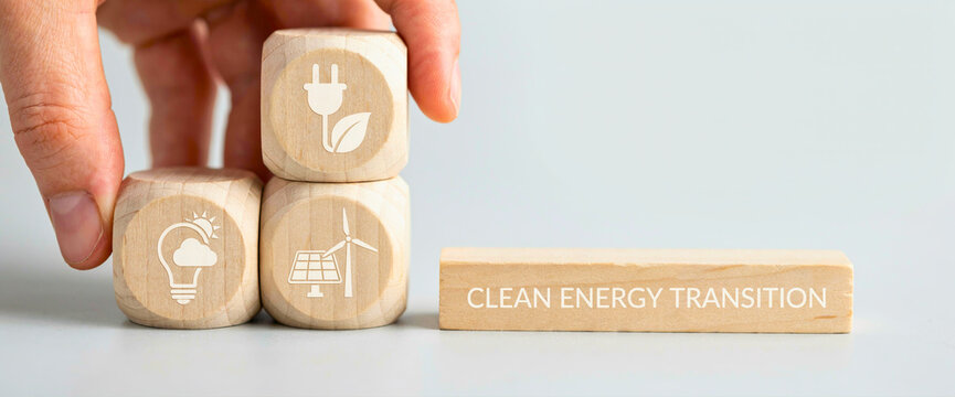 Hand arranging wooden blocks with clean energy transition text and icons promoting renewable power shift and sustainable environmental policy