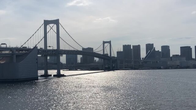 Panoramic view of the Rainbow Bridge and Tokyo cityscape with sparkling sun reflection on water surface silent