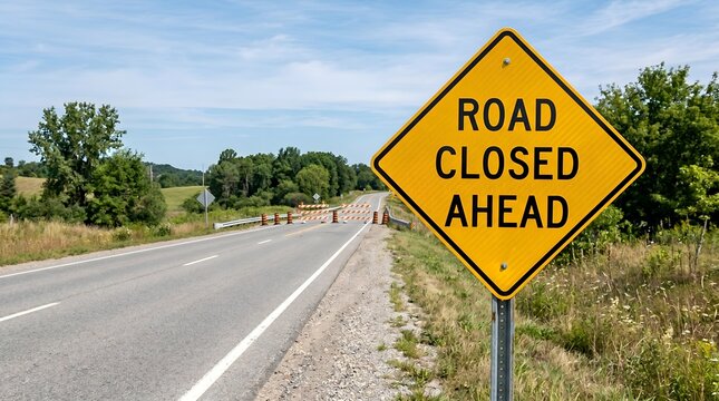 Road closed ahead sign with barricades on a sunny day with trees