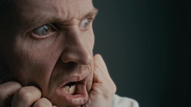 Closeup of middle aged Caucasian man suffering from severe mental breakdown, grimacing in pain and covering ears in distress. Ideal for mental health awareness campaigns and psychiatric clinic promos