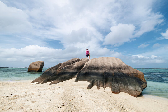 Tourist standing on top of granite rock in Seychelles and looking around at horizon. Solitude, freedom, outdoor exploration and travel destination concept.