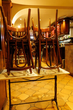 Stacks of wooden bistro chairs turned upside down on table inside closed cafe