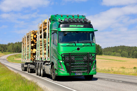 New green Volvo FH16 780 logging truck transports log load along highway on a beautiful day of summer. 