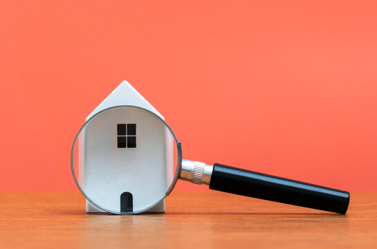 A miniature white house viewed through a magnifying glass. Real estate search, property inspection, housing market analysis, and mortgage appraisal concepts.