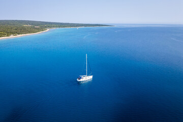 Obraz premium An aerial drone shot capturing a lone white sailboat cruising on the vibrant blue waters of the Adriatic Sea near the coast of Silba Island, Croatia. The minimalist composition emphasizes the vast