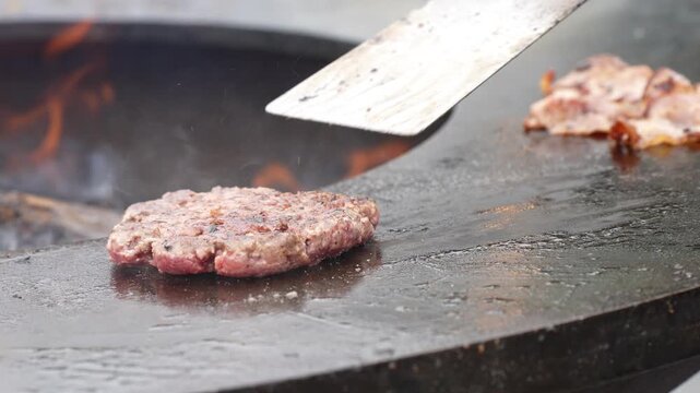Juicy barbecue burger patty sizzling on a wood fired ring roaster while chef hands cook fresh ingredients for commercial gourmet catering