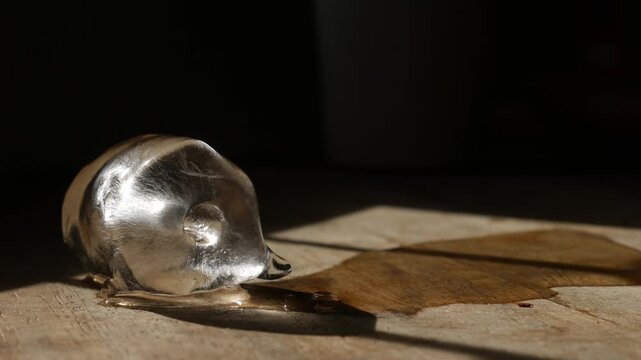 Melting ice cube with water puddle on rustic wooden table with dramatic sunlight and shadow pattern in moody still life photography