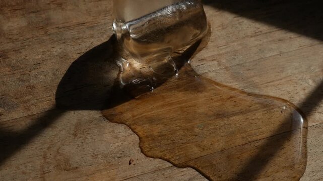 Melting ice cube with water puddle on rustic wooden table with dramatic sunlight and shadow pattern in moody still life photography
