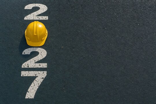 Creative 2027 construction industry concept with yellow safety helmet placed as zero on black asphalt road surface with painted white numbers marking year progress.
