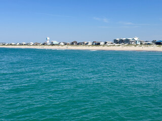 Fototapeta premium Clear turquoise waters of the Atlantic Ocean stretch toward the sandy shoreline and beachfront homes of Atlantic Beach, North Carolina on a bright summer day.