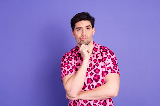 Fashionable young man wearing a pink shirt with leopard print makes a thinking gesture against a violet background