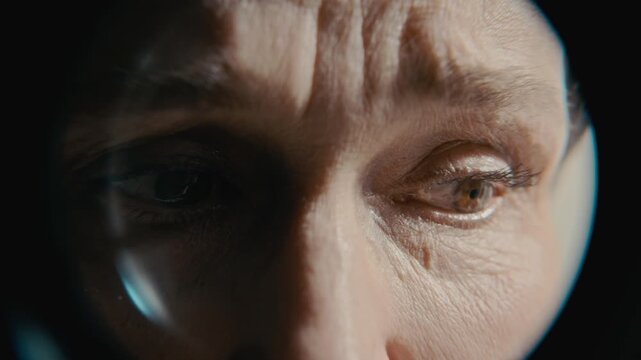 Closeup portrait of senior Caucasian woman looking through peephole with anxious expression, showing signs of paranoia. Ideal for mental health awareness campaigns or psychiatric clinic promos