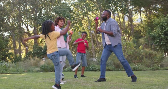 African American family dad using bubble blower, girl kicking falling rising, playing on lawn