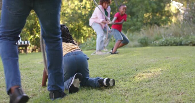 African American family playing tug war on lawn, child slipping crawling pulling rope trying to win