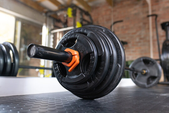 Loaded Olympic barbell resting on textured mat in gym, with stacked black plates and orange clamp
