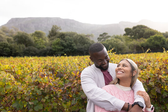 African American couple wrapping arms gazing in vineyard amid vine rows wearing watch and bracelet