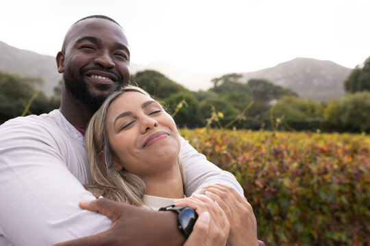 African American couple embracing in rural vineyard, man wearing smartwatch, woman in knit sweater