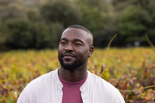 African American man standing in autumn field vegetation, gazing left, wearing maroon T-shirt