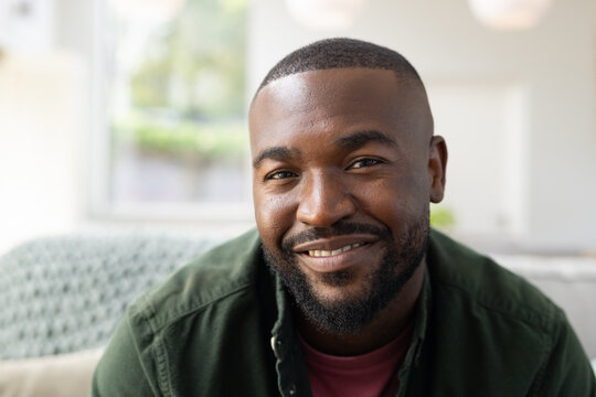 African American man sitting on couch in bright living room, smiling with knitted throw