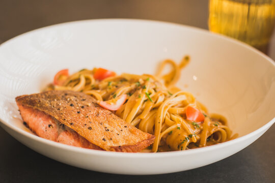grilled salmon steak with linguine paste glazed in prawn bisque in a white ceramic dish