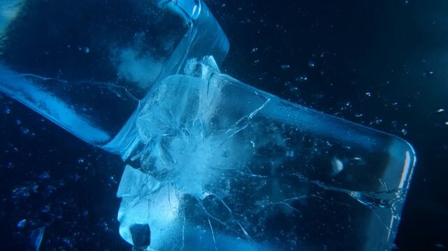 Slow motion close up of ice cubes colliding and shattering underwater in deep blue liquid tracking macro view of cracking frozen blocks