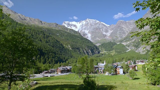 Static shot of Macugnaga alpine village in Anzasca Valley Italy with Monte Rosa glacier mountain landscape, summer panorama of Italian Alps, forests, meadows and church tower