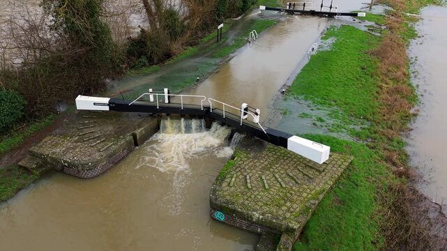 Drone perspective of intense floodwaters rushing past historical canal lock gates in Leicestershire England