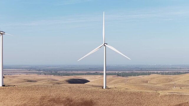 Wind turbines turning in the breeze on the rolling hills of Altamont Pass in Northern California, generating clean, renewable energy under a clear blue sky on a sunny day