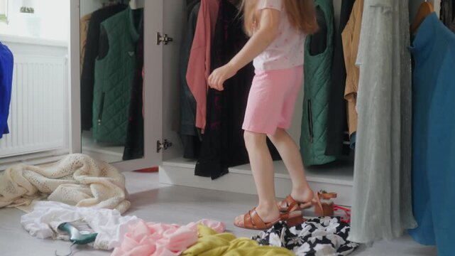 A playful girl walks in big high heel footwear near a wardrobe.