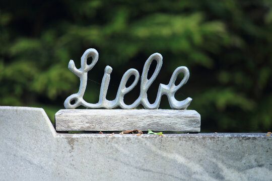 Metallene Schriftskulptur mit dem Wort Liebe vor gr&uuml;nem Naturhintergrund