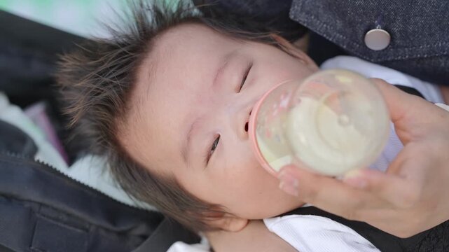 Baby sleeps peacefully while being fed from a bottle. Soft light highlights the child's calm, content expression. Hands gently hold bottle near the child's face. Ideal for parenting, child care
