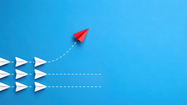Red Paper Plane Breaking Away From White Planes on Blue Background With Copy Space
