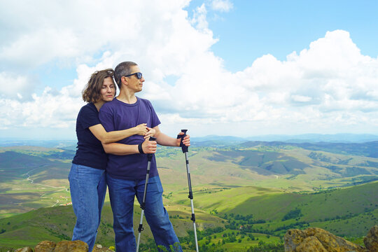 Woman nestles against her partner on summit, eyes closed, as green ridges roll out behind. Highlights intimate travel moment, shared outdoor bond, and emotional closeness through mountain adventure.