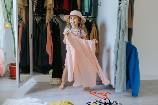 Happy young child laughing and holding a large adult blouse by a wardrobe.