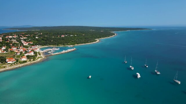 Stunning aerial view of Sotorisce Bay on the eastern shore of Silba Island, Croatia, featuring crystal clear turquoise water, a sandy seabed, and a protected harbor filled with white sailboat