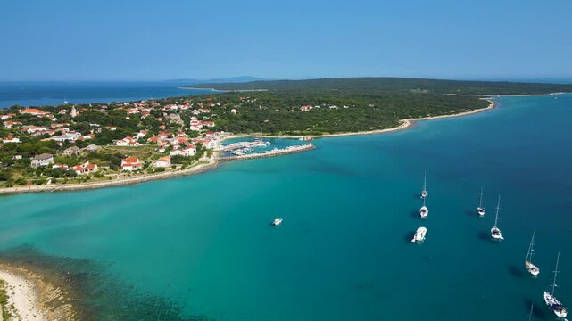 Stunning aerial view of Sotorisce Bay on the eastern shore of Silba Island, Croatia, featuring crystal clear turquoise water, a sandy seabed, and a protected harbor filled with white sailboat