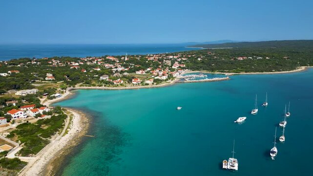 Stunning aerial view of Sotorisce Bay on the eastern shore of Silba Island, Croatia, featuring crystal clear turquoise water, a sandy seabed, and a protected harbor filled with white sailboat
