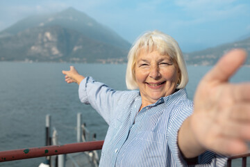 Fototapeta premium Portrait of a happy senior lady with grey hair showing beautiful landscape background on a sunny day during her retirement journey.